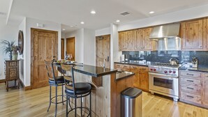 A modern kitchen with wooden cabinets, a stainless steel stove, and a bar area with stools. - Shooting Star Lodge at Deer Valley Resort - Two Bedroom Residence #203 2 Condo (Park City)