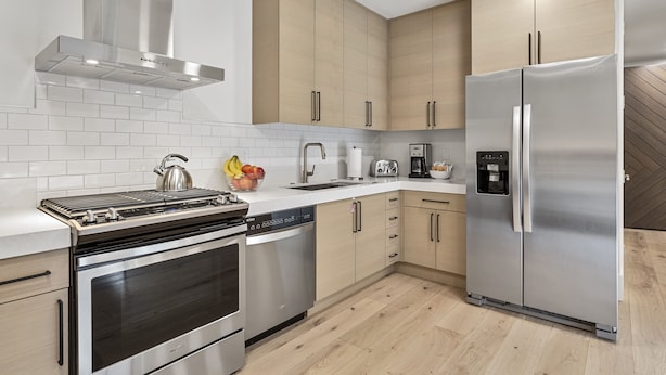 Una cocina moderna con electrodomésticos de acero inoxidable, armarios de madera y salpicadero de azulejos.