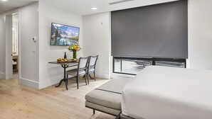 Un dormitorio moderno con una cama grande, una mesa de comedor con sillas, un cuadro y vistas a través de una ventana.