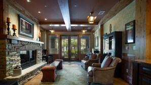 A cozy living room with a stone fireplace, leather sofas, and a large window offering a view of the outdoors.