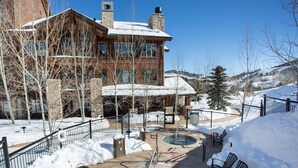A hotel with a stone facade, two outdoor hot tubs, and a snow-covered landscape.