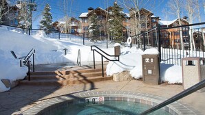 A hot tub area with steps leading up to a building, surrounded by snow and trees.