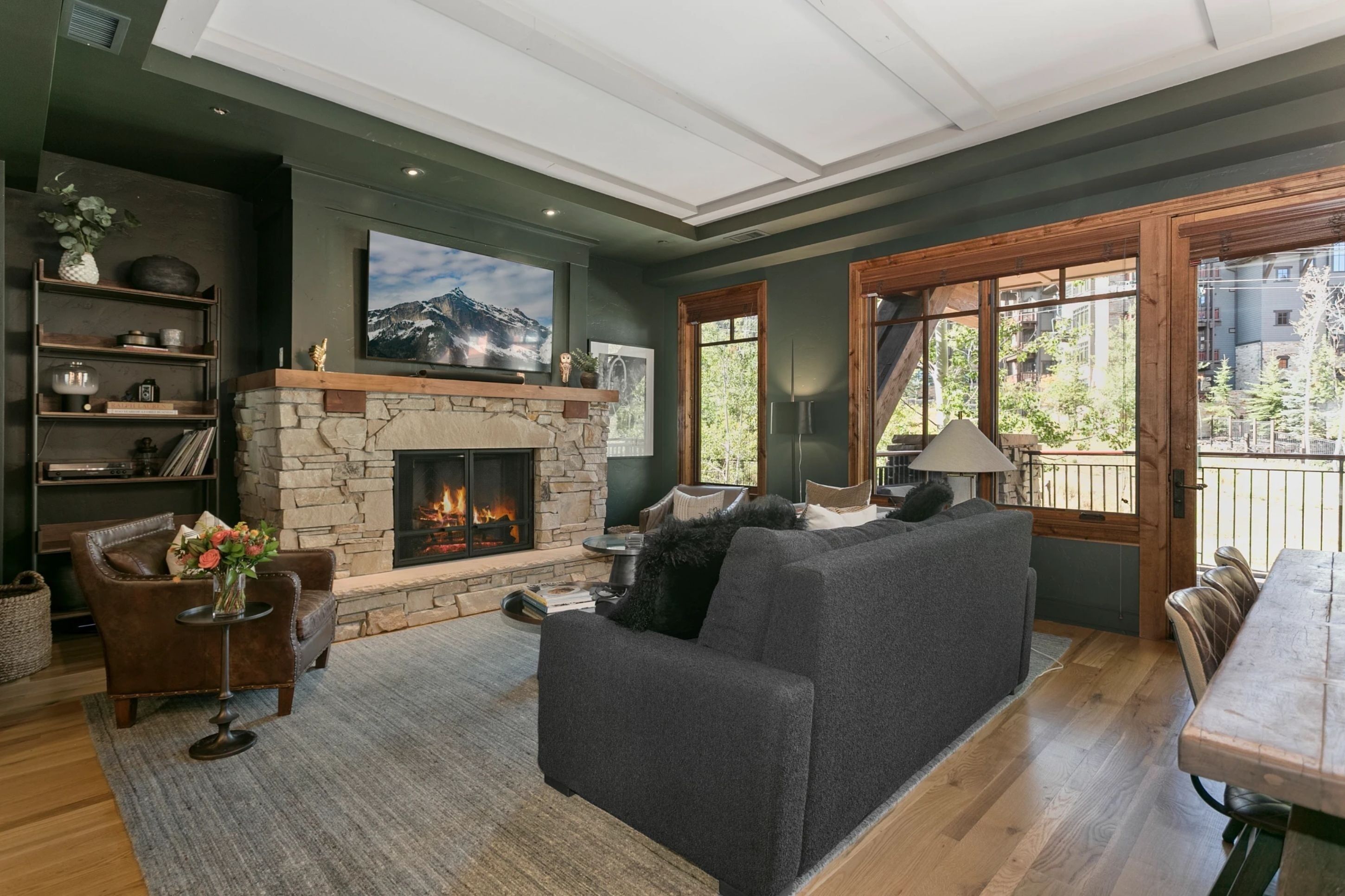 Una sala de estar acogedora con chimenea de piedra, un televisor de pantalla plana grande, un sofá gris y una mesa de comedor de madera.