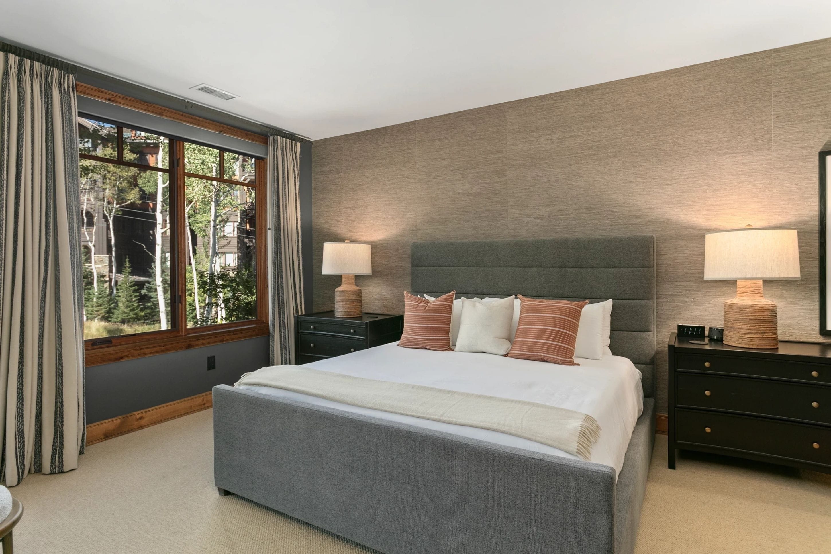 Habitación de hotel con una cama grande, dos mesitas de noche, una ventana con cortinas y vistas a árboles.
