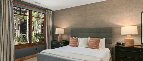 Habitación de hotel con una cama grande, dos mesitas de noche, una ventana con cortinas y vistas a árboles.