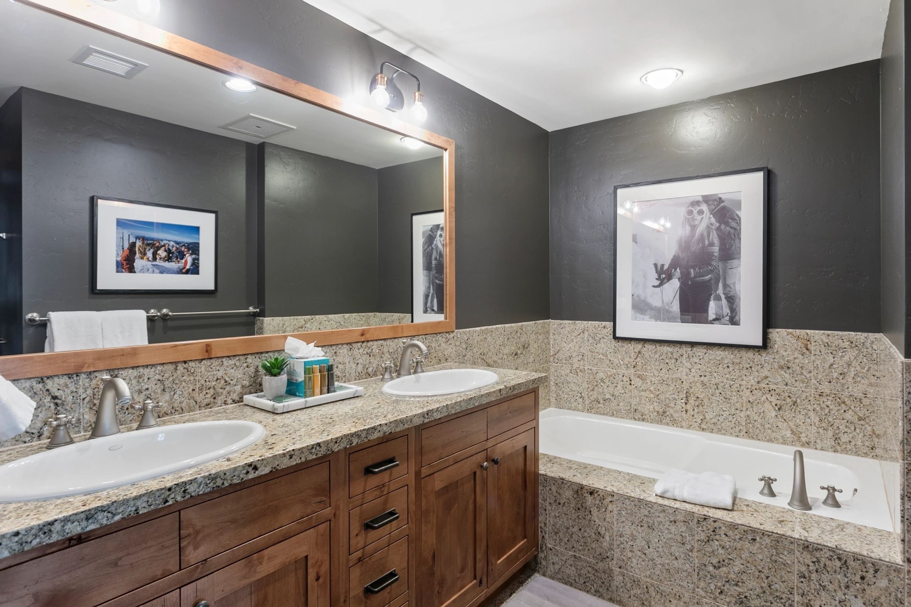 A modern bathroom with two sinks, a large mirror, and a bathtub.