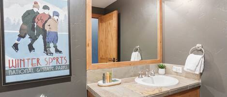 Un baño con un espejo grande, un lavabo, un perchero para toallas y un cartel con atletas de deportes de invierno.