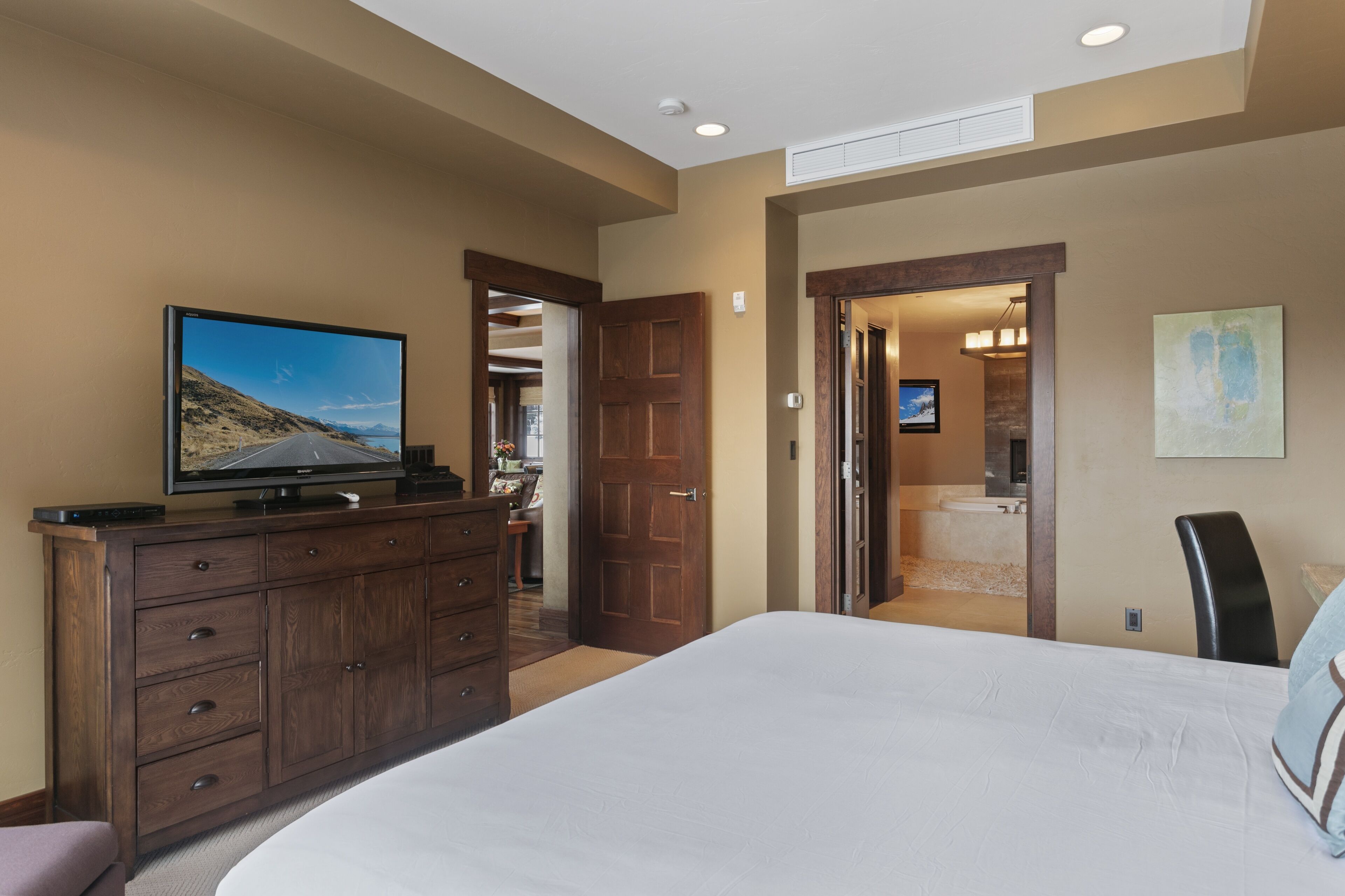 Un dormitorio con una cama grande, un aparador, un televisor y una puerta que da a un baño.