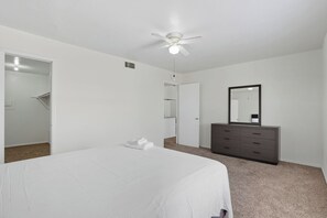 A bedroom with a bed, a dresser, a ceiling fan, and a mirror.