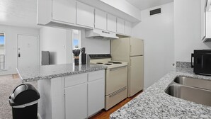 A modern kitchen with white cabinets, a granite countertop, a stove, a refrigerator, and a trash can. - Apt. In college station TX. Mins to major hospitals and A&M U (College Station)