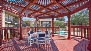 A covered outdoor area with a wooden deck, a table with chairs, and a pool in the background. - Apt. In college station TX. Mins to major hospitals and A&M U (College Station)