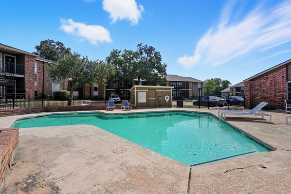 A rectangular swimming pool with two lounge chairs and a small building in the background.
