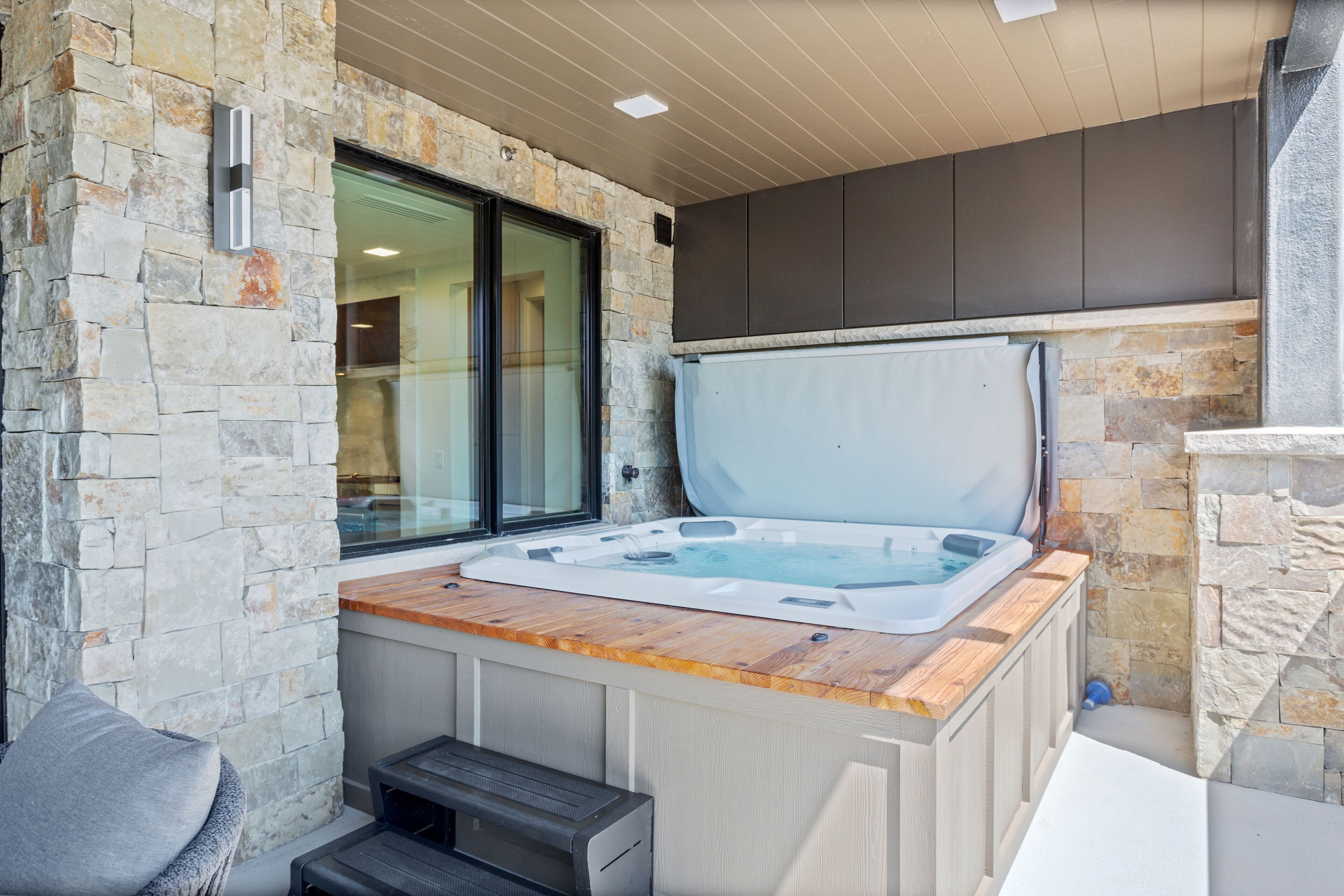 A stone exterior wall, a wooden deck, and a hot tub.