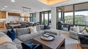 Un salon moderne doté d’un grand canapé d’angle, d’une table basse et d’un coin repas avec une grande fenêtre donnant sur la campagne.