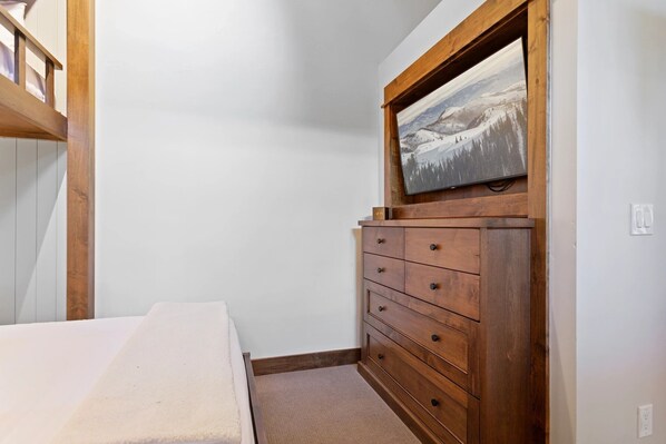 A bedroom with a bunk bed, a wooden dresser with drawers, and a framed picture on the wall.