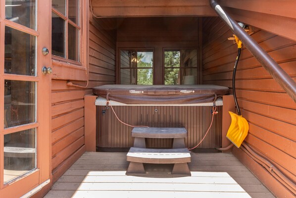 Una cabaña de madera con jacuzzi, banco y puerta con ventanas.