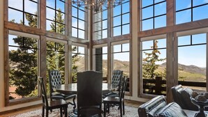 A dining area with a large table and chairs, large windows with a view of trees and hills. - Stag Lodge at Deer Valley Resort - Three Bedroom Residence with Spa #13 3 Condo (Park City)