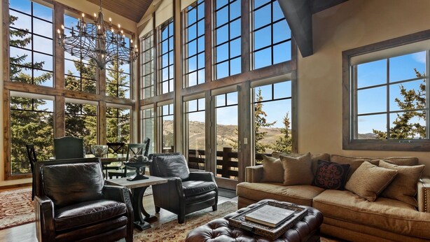 A spacious living room with large windows, leather furniture, and a chandelier. - Stag Lodge at Deer Valley Resort - Three Bedroom Residence with Spa #13 3 Condo (Park City)