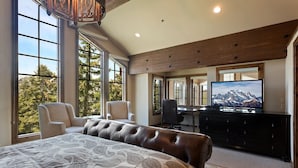 A bedroom with a large bed, two chairs, a desk, a television, and a view of trees through large windows. - Stag Lodge at Deer Valley Resort - Three Bedroom Residence with Spa #13 3 Condo (Park City)
