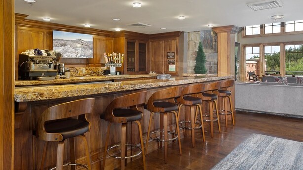 A spacious kitchen with a granite countertop, wooden bar stools, and a large window offering a view of the outdoors.