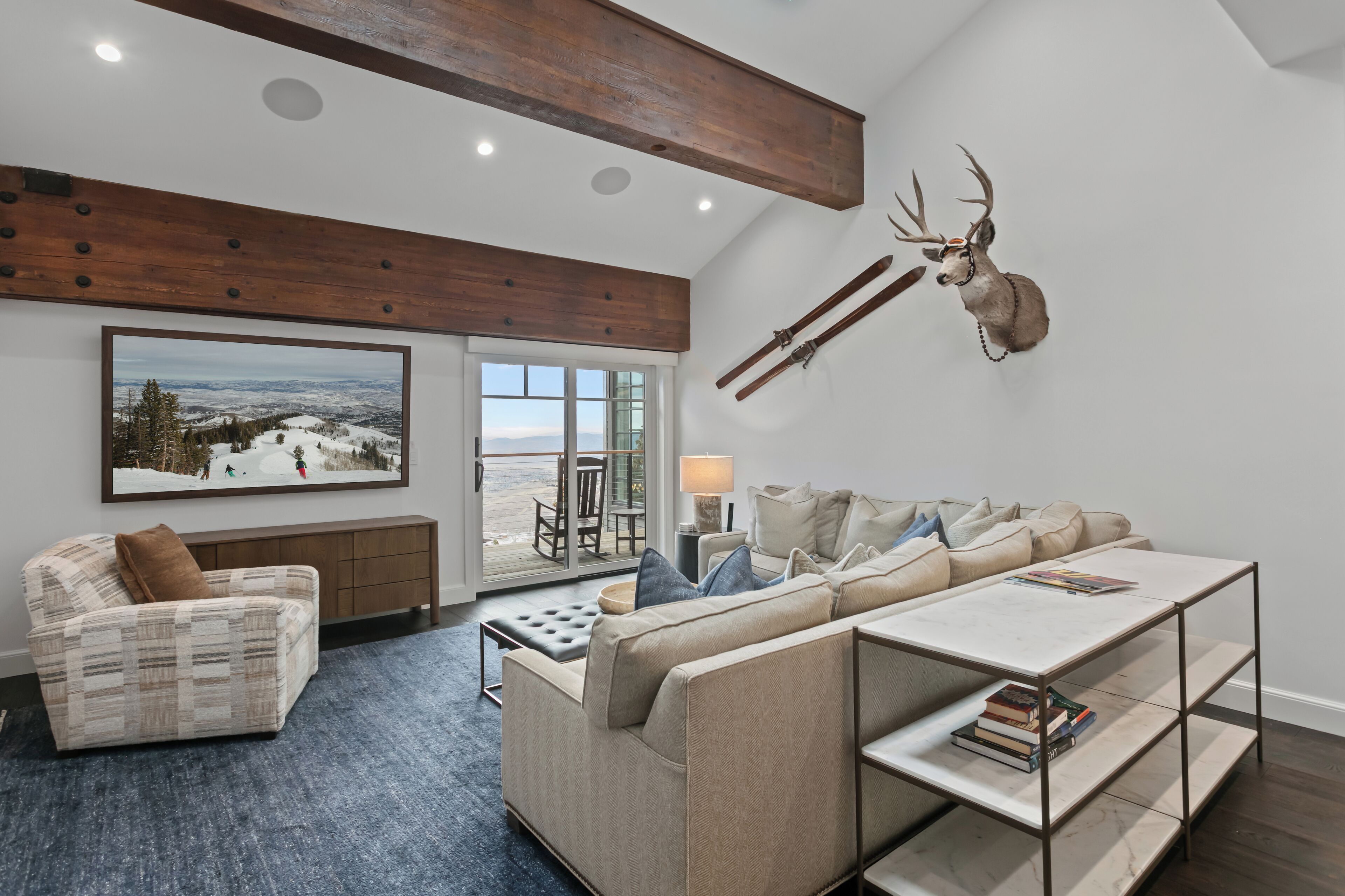 A living room with a large window, a mounted deer head, a sofa, a coffee table, and a bookshelf.