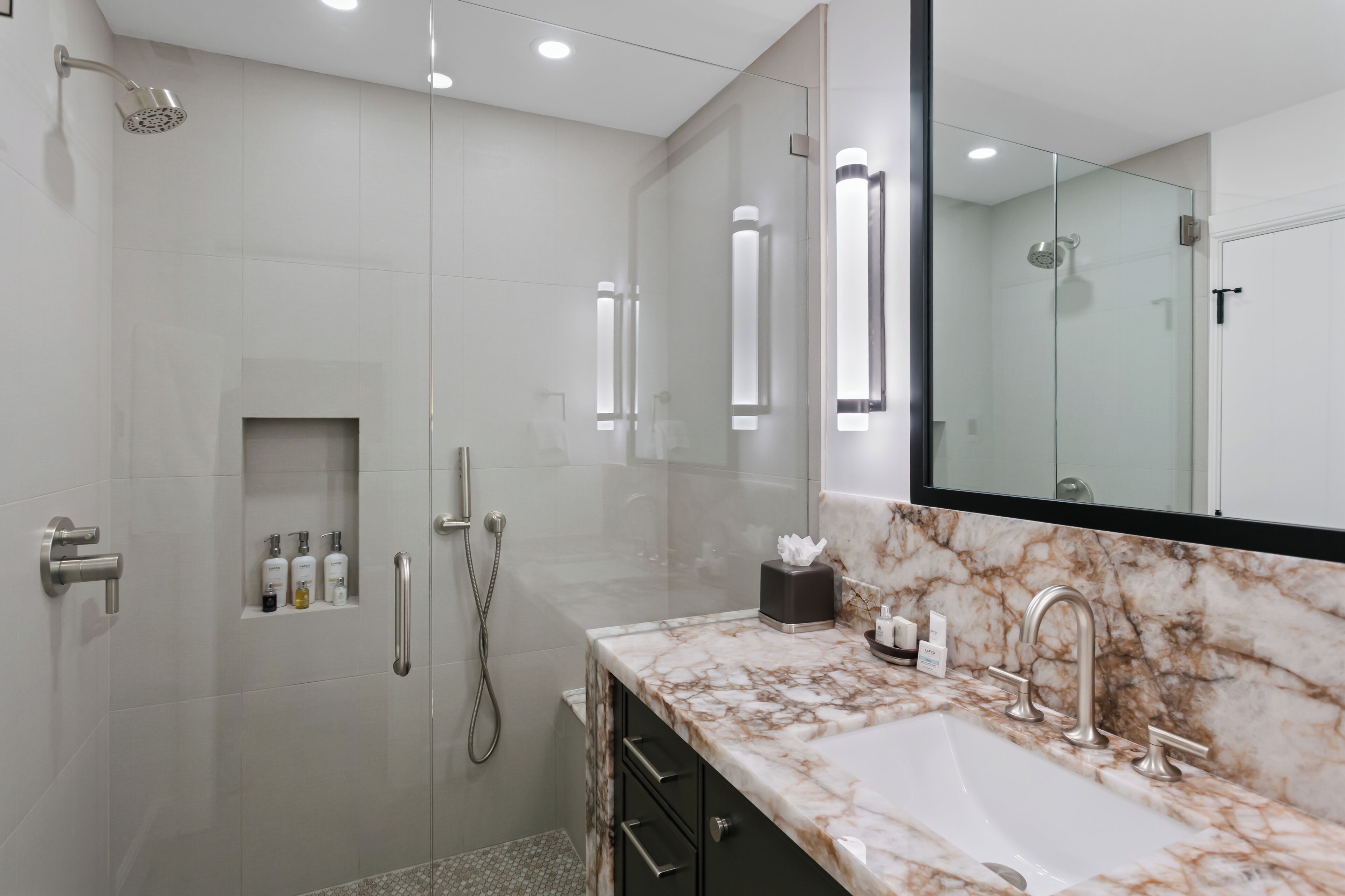 Une salle de bain moderne avec une douche à parois de verre, un lavabo en marbre et un grand miroir.