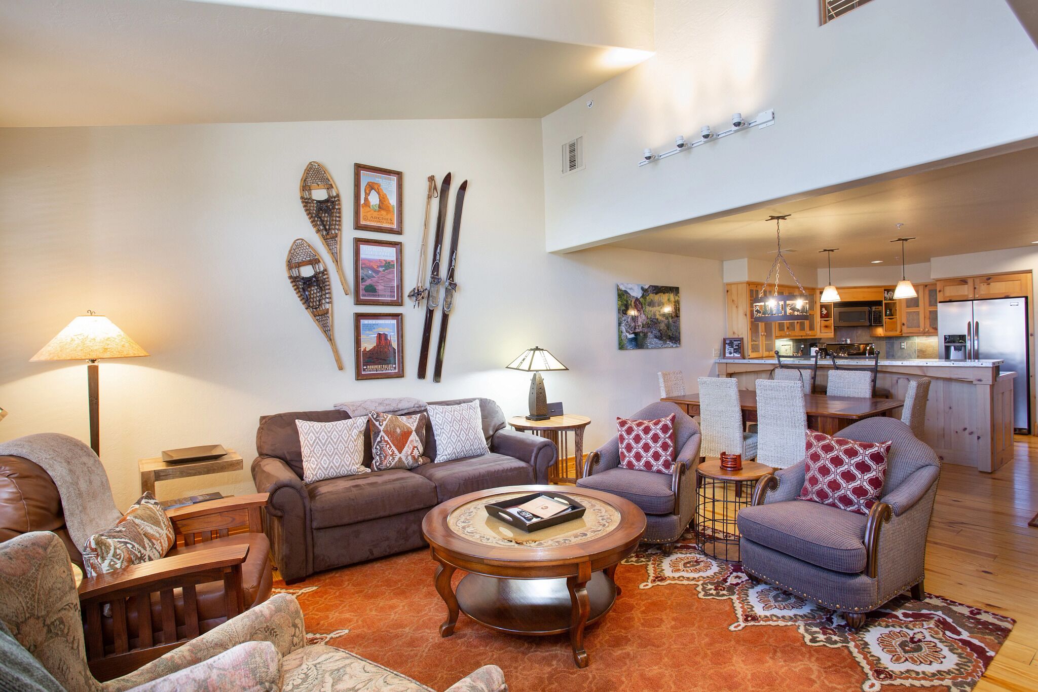 A living room with a sofa, armchairs, a coffee table, and a rug. There are framed pictures on the wall and a pair of skis hanging.