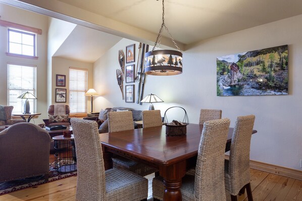 A dining area with a wooden table and woven chairs, a chandelier, and a painting on the wall. - The Lodges at Deer Valley 3 Bedroom Condo (Park City)