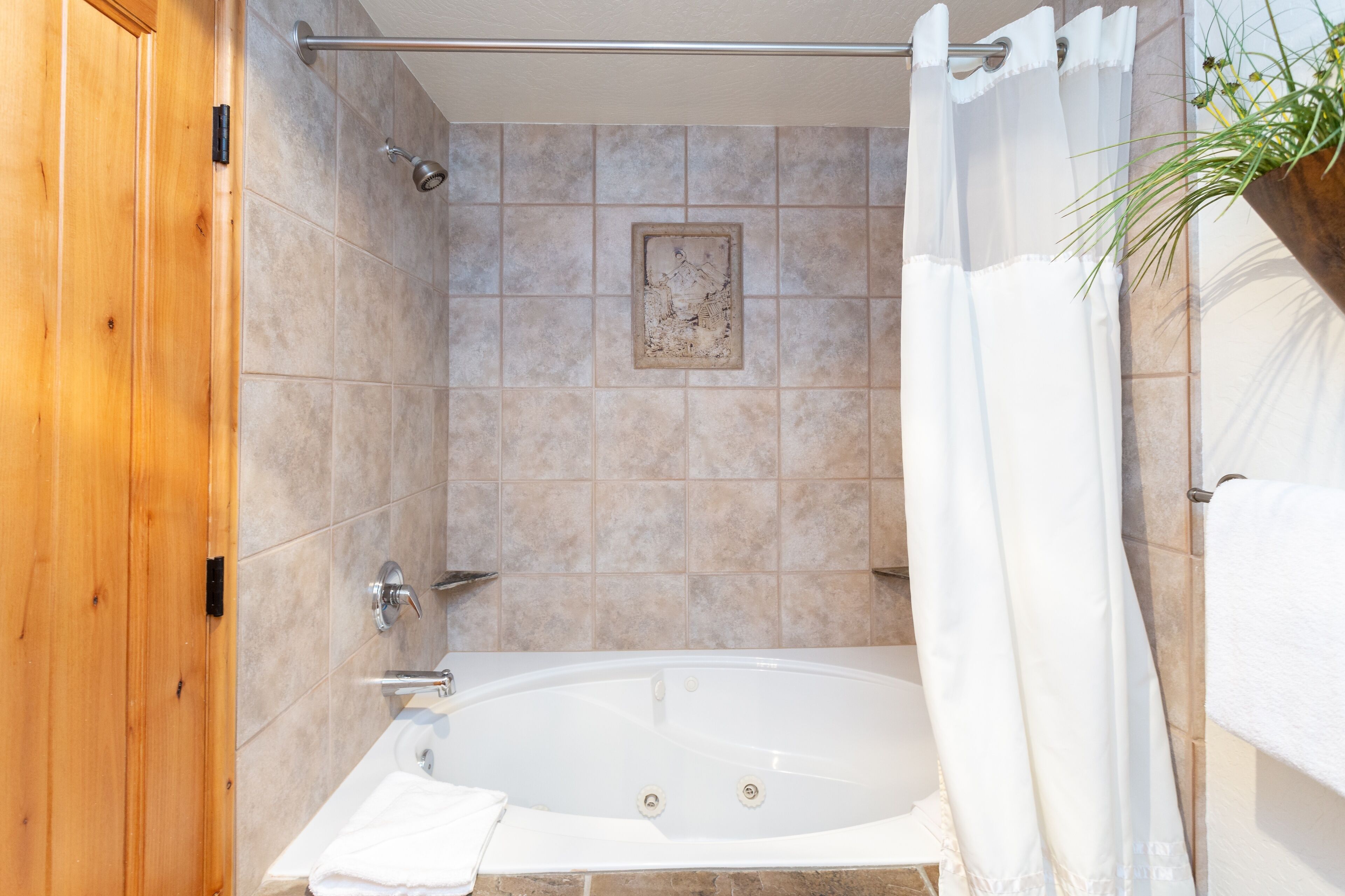 A bathroom with a bathtub, wooden door, tiled walls, and a shower curtain.