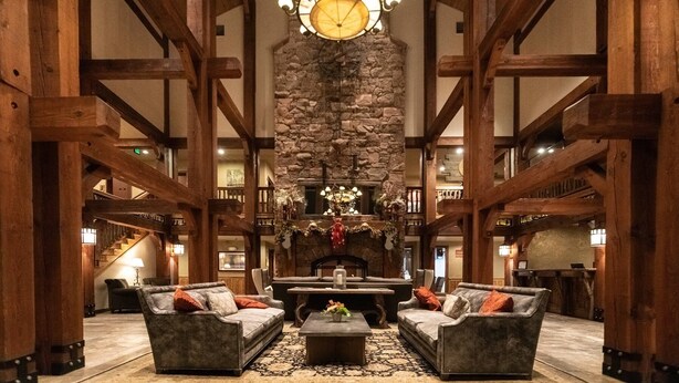 A spacious lobby with high wooden beams, a stone fireplace, and a large clock on the wall.