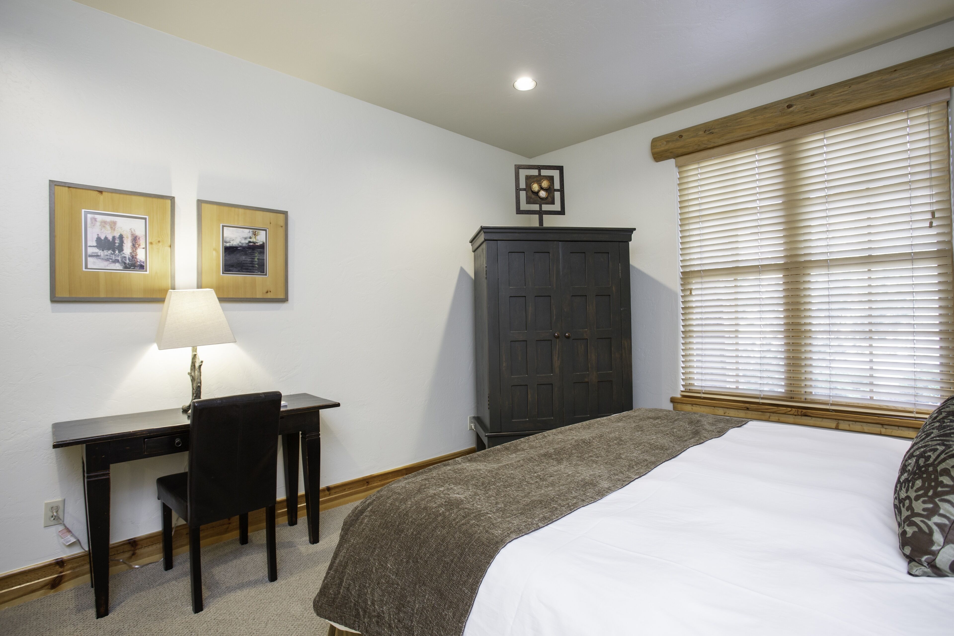Une chambre à coucher comprenant un lit, un bureau avec une chaise, une armoire et deux tableaux encadrés accrochés au mur.