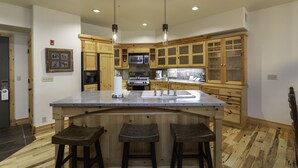 A kitchen with wooden cabinets, a central island with stools, a microwave, and a sink.