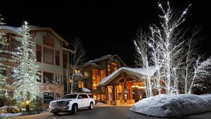 A multi-story hotel with a prominent entrance, snow-covered landscape, and a white SUV parked in front.
