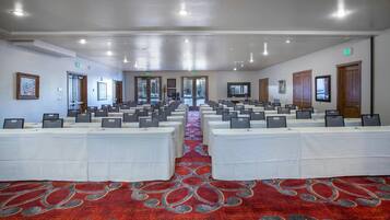 Un salón de conferencias con filas de mesas y sillas, una alfombra roja y señales de salida.