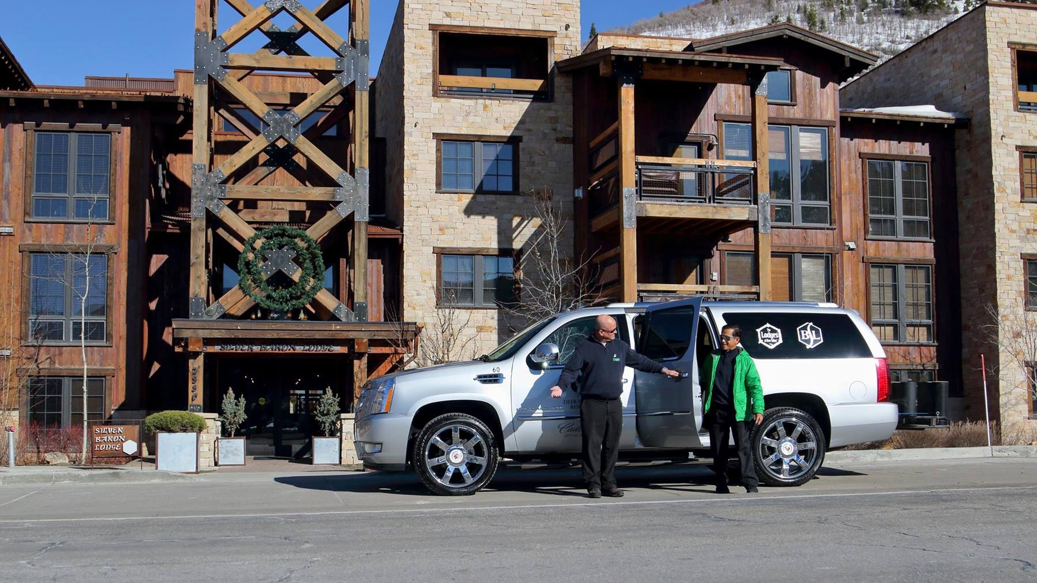 A white SUV parked in front of a lodge with a wooden facade and a large cross-braced structure.