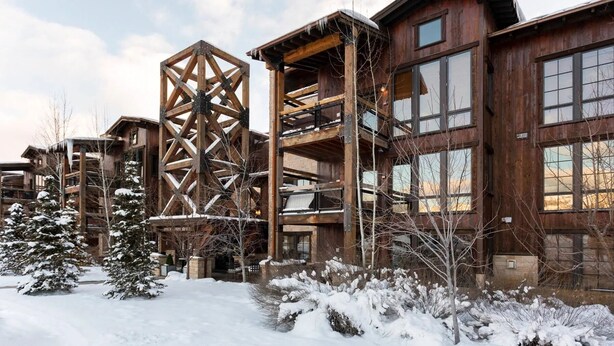 Un edificio de madera de varios pisos con una estructura de celosía singular, rodeado de suelo y árboles cubiertos de nieve.