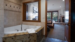 Un baño con una bañera grande, un espejo y vistas a un dormitorio a través de una puerta abierta.