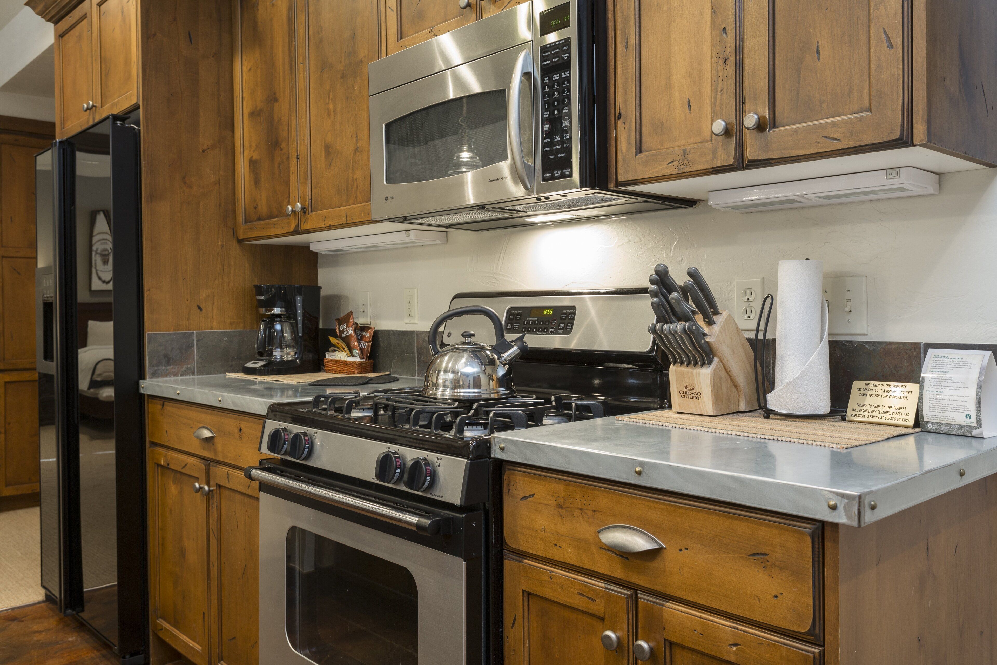 A kitchen with wooden cabinets, a stainless steel microwave, a gas stove, and a coffee maker.