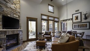 A living room with a stone fireplace, leather sofa, and a large window with blinds.