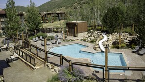 A pool area with a slide, lounge chairs, and a view of a mountain.