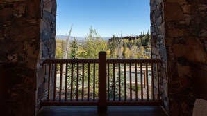 A stone-walled balcony with a wooden railing overlooking a scenic view of trees and mountains.
