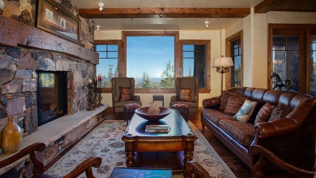 A cozy living room with a stone fireplace, leather sofa, and a large window offering a scenic view.