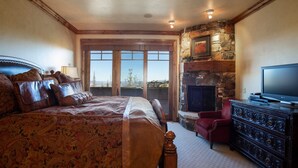 A bedroom with a large bed, a stone fireplace, a television, and a red chair.