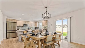 A modern kitchen with stainless steel appliances, a dining area with wooden chairs and a table set for four, and a large sliding glass door leading to a patio. - Spacious 6BR Sleeps 22 with Playground, Basketball (Nampa)