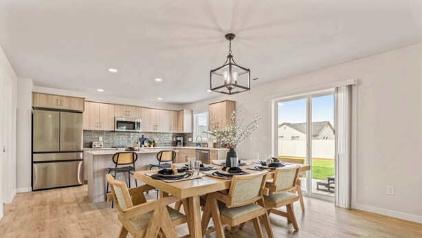 A modern kitchen with stainless steel appliances, a dining area with wooden chairs and a table set for four, and a large sliding glass door leading to a patio.