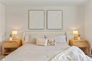 A bedroom with a large bed, two bedside tables, and two wall-mounted abstract paintings.