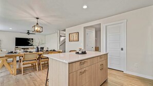 A modern kitchen with wooden cabinets, a white countertop, and a dining area with a wooden table and chairs.