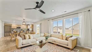 A spacious living room with a sectional sofa, a glass coffee table, and a large window with blinds.