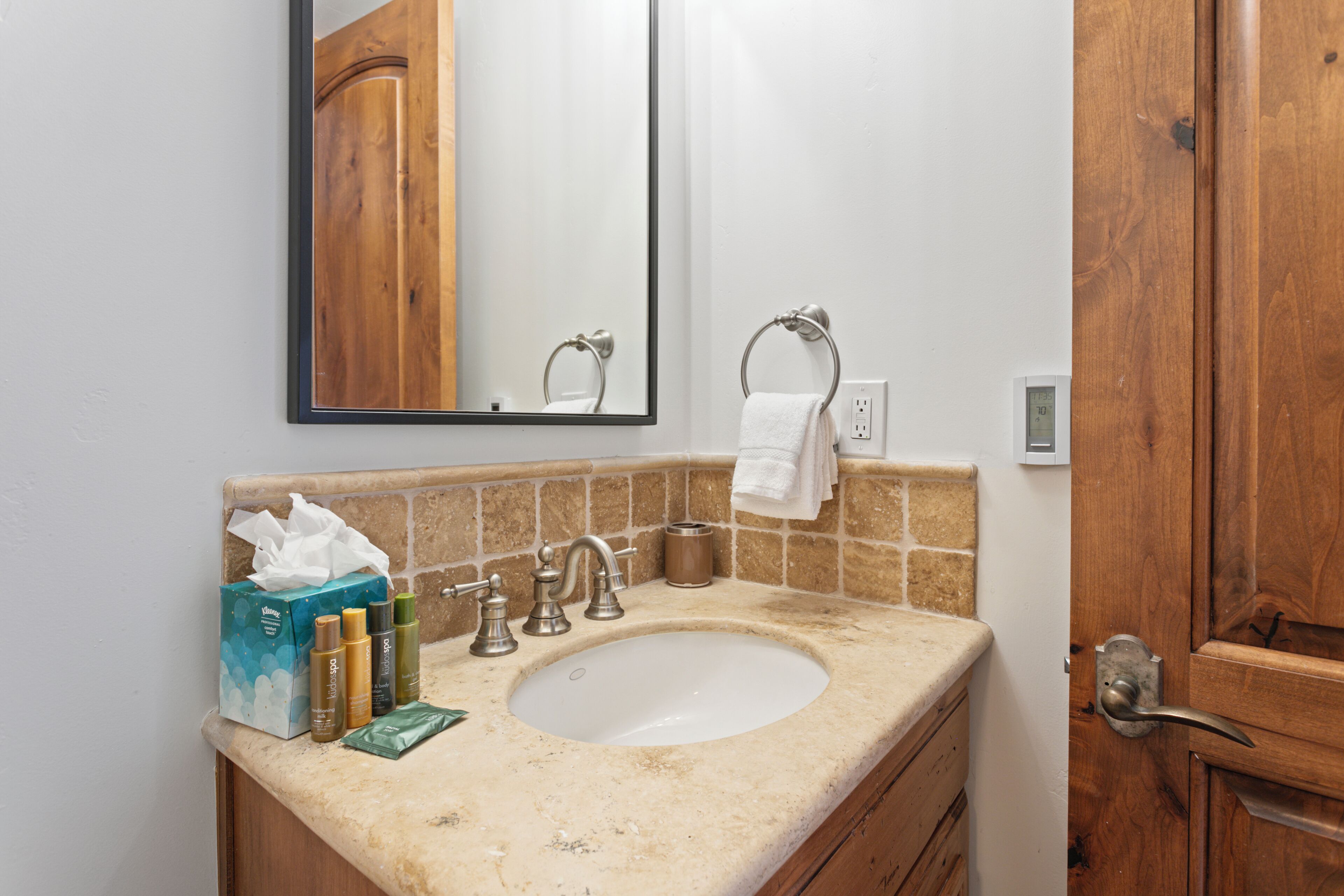 A bathroom with a sink, mirror, towel ring, and toiletries.