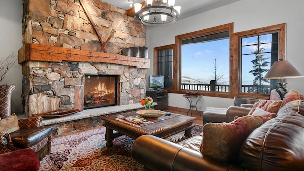 A cozy living room with a stone fireplace, leather furniture, and large windows offering a view of the outdoors. - Grand Lodge - 3 Bedroom Condo Deluxe #206 - Ski-in/out by Deer Valley Resort (Park City)
